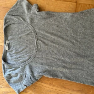 Grå ribbad t-shirt med rund hals - En enkel och stilren grå t-shirt med ribbad struktur och rund, djup urringning. T-shirten har korta ärmar och är perfekt för en avslappnad look. Passar till det mesta och är lätt att matcha med andra plagg.