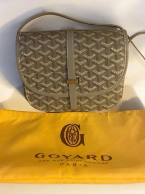 Beige axelväska  - Snygg beige axelväska med klassiskt mönster och justerbar axelrem. Väskan har lock med spänne och detaljer i läder. Kommer med original dustbag i gult tyg. Perfekt för dig som gillar exklusiva accessoarer.