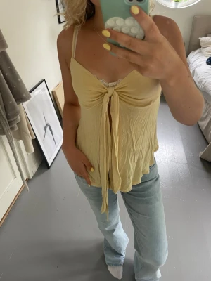 Gul linnetopp med knyt  - Supersöt ljusgul linnetopp från Gina Tricot med knyt framtill och lätt v-ringad hals. Toppen är ärmlös och har en flowy passform, perfekt till jeans eller kjol. Materialet känns mjukt och luftigt, perfekt för varma dagar.