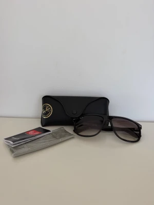 Svarta Ray-Ban solglasögon - Snygga svarta Ray-Ban solglasögon med mörka glas. Kommer med originalfodral, putsduk och etikett. Perfekta för att höja din stil på sommaren eller när solen skiner. Helt nya