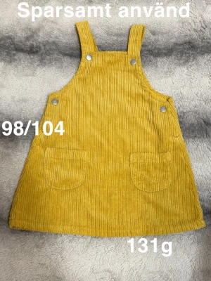 Gul manchesterkjol med hängslen - Gul kjol i manchester med breda hängslen och två stora fickor framtill. Kjolen har en rak och loose passform samt ribbad struktur. Perfekt att bära med en t-shirt eller tröja under för en avslappnad look.🌸 Sparsamt använd. Storlek 98/104