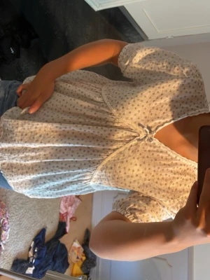 Vit blommig blus från Kappahl - Söt vit blus från Kappahl med små blommönster i grått och puffiga korta ärmar. Blusen har en knytning framtill och är gjord i ett tunt, luftigt material som känns perfekt för sommaren. Passar dig som gillar romantisk och avslappnad stil.