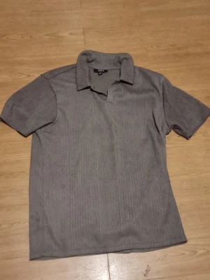 Grå brun polotröja - INSTABOX!!! Säljer en stilren grå brun polotröja med korta ärmar och ribbad struktur. Tröjam har klassisk krage och en relaxed passform, perfekt för dig som gillar enkel men snygg stil. Materialet känns mjukt och bekvämt mot huden. XS i herr storlek 
