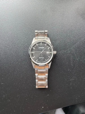 Citizen silverfärgad klocka - Stilren klocka från Citizen med silverfärgad länk i metall och svart urtavla. Urtavlan har tydliga markeringar, datumvisning och en klassisk rund form. Perfekt accessoar för dig som gillar en tidlös look.