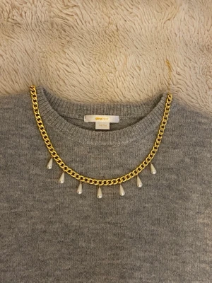 Guldhalsband med droppformade pärlor - Snyggt halsband i guldfärgad kedja med hängande droppformade pärlor. Kedjan har en chunky känsla och pärlorna ger en elegant touch. Perfekt för att lyfta vilken outfit som helst med lite extra bling.