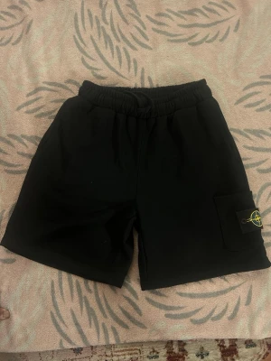 Stone Island shorts.  - Säljer ett par svarta shorts från Stone Island med elastisk midja och en ficka på sidan med den klassiska loggan. Perfekta för sommaren och riktigt sköna att bära. Passar till allt och har en clean look. De har storlek S/M