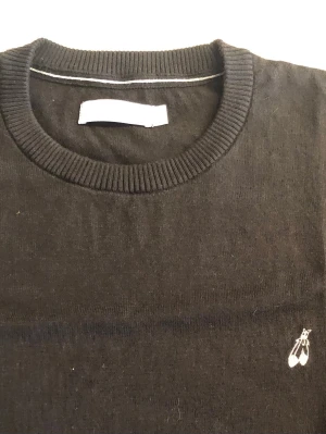 Svart Peak Performance stickad tröja med brodyr - Enkel och stilren design, perfekt för lager på lager under kyliga dagar.