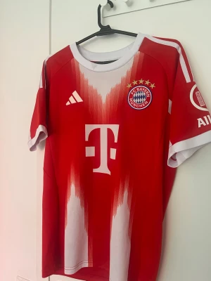 Bayern München matchtröja Olise - Säljer en röd och vit Bayern München matchtröja  med klubbmärke och sponsortryck på bröstet. Tröjan har korta ärmar, rund hals och vita detaljer längs sidorna och axlarna med Olise nmr17 på ryggen. Perfekt för fotbollsfans som vill stötta sitt lag. Använd några gånger men ganska bra skick. Hör av er vid funderingar!
