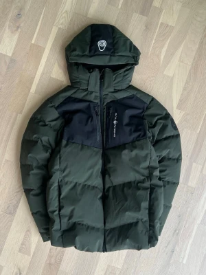 Sail Racing Olivegreen jacket size 176 - Excellent condition. Warm, lightweight and stylish winter jacket with adjustable hood, full front zipper, two chest zip pockets and two side pockets. Windproof and water-resistant. Perfect for everyday wear and outdoor activities. Genuine Sail Racing quality. Retail = 350$ USD
