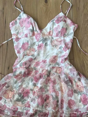 hollister blomster kjole - ubrukt søt kjole med tynne stropper og V-hals. Kjolen har et romantisk blomstermønster i rosa, grønt og beige på hvit bunn. Skjørtet er lett utsvingt og stoffet føles luftig – perfekt for varme dager.