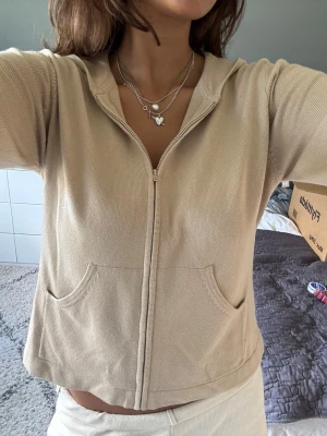 Beige hoodie med dragkedja - Säljer en beige hoodie med dragkedja, två fickor och huva. Passar till det mesta och är superskönt. Köpt second hand 