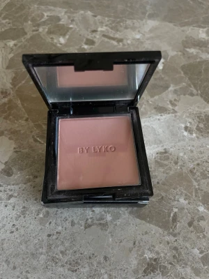 Blush Peach - Säljer ett Très Cheek Blush från Lyko i en mjuk, matt rosa nyans. Rouget kommer i en stilren fyrkantig dosa med spegel i locket, perfekt att ha med i väskan. Pudret har en pressad form.