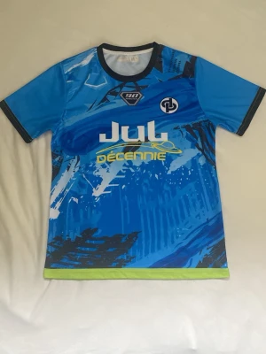 Jul t shirt - Säljer en blå Jul t shirt med coolt grafiskt tryck i olika blå nyanser, vitt och svart. Tröjan har korta ärmar, svarta detaljer vid hals och ärmslut samt limegrön kant nertill. Perfekt för träning eller lagaktiviteter.