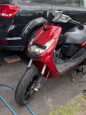 Kåpor  - En röd Peugeot scooter med svart sits och detaljer. Scootern har sportig design, stora framlyktor och svarta handtag. Märket Polini syns på sidan av sitsen. Perfekt för dig som vill ha ett smidigt fordon.