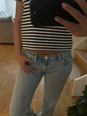 Ljusblå raka jeans med hög midja - Säljer ett par ljusblå jeans med rak passform och hög midja. Jeansen har klassisk femficksdesign, knappgylf och är tillverkade i denim. Perfekta för en avslappnad och trendig look.