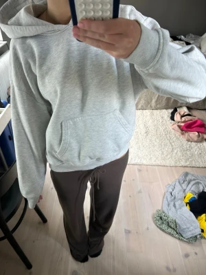 Ljusgrå hoodie från Gina - En basic ljusgrå hoodie med huva och stor magficka. Hoodien har ribbade muddar vid ärmslut och nederkant samt en avslappnad passform. Perfekt för chill dagar eller när du vill ha något bekvämt och enkelt. Materialet känns mjukt och skönt mot huden.