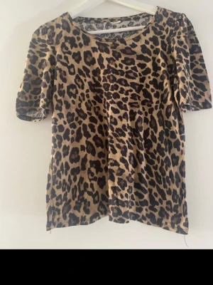 Leopardmönstrad topp med puffärm - Snygg topp med leopardmönster i beige och svart. Modellen har rund halsringning och korta puffärmar som ger en trendig look. Perfekt för dig som vill sticka ut lite extra. Materialet känns mjukt och följsamt mot huden.