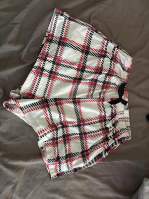 Rutiga pyjamasbyxor och shorts - Säljer ett set med rutiga pyjamasbyxor och matchande shorts i vitt, rött och svart. Båda har ett elastiskt midjeband med svart rosett framtill. Perfekt för mysiga hemmakvällar. Materialet känns mjukt och bekvämt mot huden.