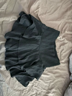 Svart volangkjol med bred midja - Säljer en svart kjol med dubbla volanger och bred resår i midjan. Kjolen har en kort och luftig modell som ger en trendig och ungdomlig look. Perfekt att matcha med en crop top eller stickad tröja.