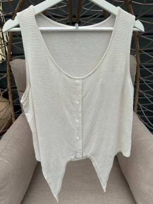 Randig ärmlös linnetopp från ONLY - Säljer en ljus, ärmlös linnetopp från ONLY med tunna beige ränder och knappar framtill. Toppen har en avslappnad passform och knytning framtill. Perfekt för varma dagar och enkel att styla med jeans eller shorts.