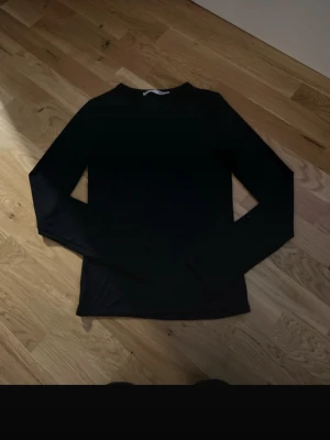 Svart långärmad topp - En enkel och stilren svart långärmad topp med rund hals. Tillverkad i ett mjukt och stretchigt material som sitter skönt på kroppen. Perfekt att matcha med jeans eller kjol för en clean look.
