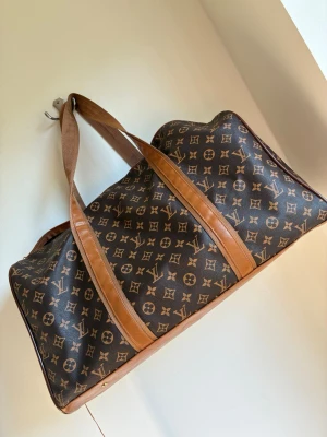  resväska weekendbag  - Snygg resväska i klassiskt brunt monogrammönster. Väskan har bruna läderdetaljer och långa handtag, perfekt för weekendresor.