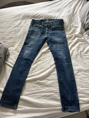 Mörkblå Lee Jeans - Snygga mörkblå Lee jeans med klassisk femficksdesign och diskreta slitningar framtill. Jeansen har normal midja och raka ben, perfekta för en trendig och avslappnad look.