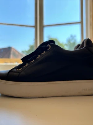 Svarta lädersneakers med vit sula från Shoe the bear, storlek 36 - Stilrena svarta lädersneakers med inbyggd platå, lågt skaft och vita sulor. Skorna har svarta skosnören och metallfärgade öljetter. Storlek 36. Supersköna!