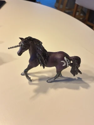 Lila enhörning med glitter - Säljer en lila enhörningsfigur i plast med glittrande man och svans. Den har ett silverfärgat horn och detaljer som en måne på sidan. 