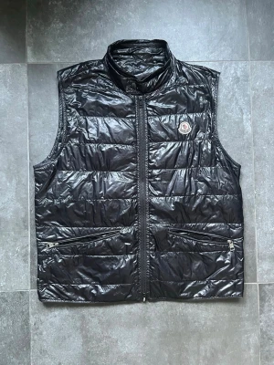 Moncler gui väst  - Tjena, säljer nu denna riktigt snygga och populära Moncler västen, den är i använt skick, tunt med dun och replacment zipper i mitten, utöver det fint skick, storlek 3/ L, hör av er vid frågor och funderingar🙌🤝 