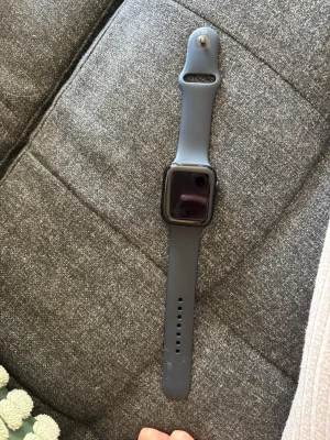 Apple watch 44 mm - Stilren svart smartklocka med rektangulär skärm och mjukt silikonarmband. Klockan har en modern design med rundade hörn och en knapp på sidan för enkel navigering. Perfekt för dig som vill ha koll på notiser och hälsa direkt på handleden.
