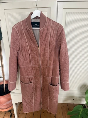 Rosa quiltad cardiganjacka från DAY-strl 34 - Lång, quiltad cardiganjacka i dust-rosa nyans från DAY. Jackan har dragkedja framtill, två stora fickor och ribbade detaljer vid krage och ärmslut. Snyggt mönstrad med sömmar och perfekt för lager på lager under kyliga dagar.