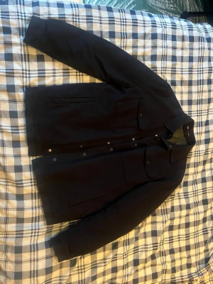 Mörklbå Zara Vinter-Overshirt - Stilren mörkblå vinter-overshirt med quiltat, olivgrönt innerfoder från Zara. Jackan har två stora bröstfickor med lock och knappar samt två sidofickor. Klassisk krage och tryckknappar framtill ger en clean look. 
