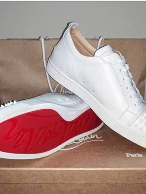 Vita sneakers med nitar och röd sula - Stilrena vita sneakers i läder med ikonisk röd sula och coola nitar på tån. Skorna har lågt skaft och klassisk snörning. Perfekta för dig som vill sticka ut med en edgy detalj och samtidigt hålla det clean.
