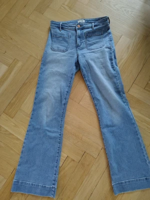 Ljusblå bootcut jeans från Wrangler - Säljer ett par ljusblå bootcut jeans från Wrangler med hög midja och raka ben. Jeansen har två stora framfickor och klassisk knappstängning med Wrangler-logga. 