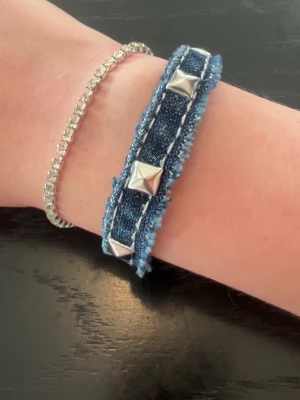 Denimarmband med nitar - Snyggt armband i mörkare demintyg, det har nitar längst hela och är lite fransig runt kanterna. Det har tryck knappar så att man kan stänga det. Det är lätt att sätta på själv, och passar till många stilar. Skriv till mig vid frågor💕