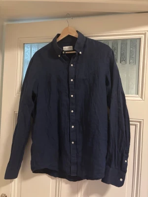 Mörkblå linneskjorta John Henric - Snygg mörkblå skjorta i linne med klassisk krage och vita knappar hela vägen framtill. Skjortan har lång ärm och en avslappnad passform, perfekt för en stilren look.