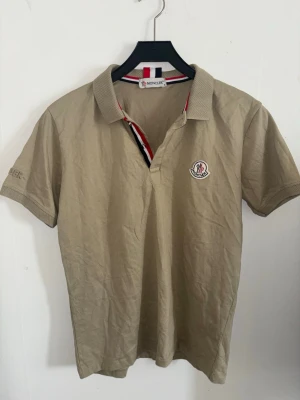  Moncler skjorta/ T-shirt  - Snygg skjorta från Moncler med klassisk krage och korta ärmar. Tröjan har Moncler-logga på bröstet och detaljer i rött, vitt och svart vid kragen. Perfekt för en clean och stilren look. Pris går att diskuteras