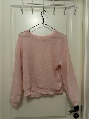 Ljusrosa stickad tröja - Mysig ljusrosa stickad tröja med rund halsringning och långa ärmar. Tröjan har en avslappnad passform och ribbade muddar vid ärmslut och nederkant. Smått genomskinlig och några noppror.
