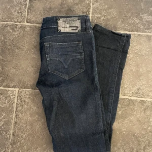 Diesel mörkblå jeans W25 L32 - Snygga mörkblå jeans från Diesel. Klassisk femficksdesign med diskret Diesel-logga på myntfickan. Jeansen har rak passform och är tillverkade i slitstarkt denimtyg. Perfekt för dig som gillar stilrena och tidlösa jeans.