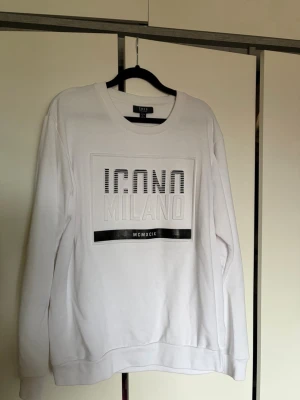 Vit sweatshirt från SMOG - Snygg vit sweatshirt från SMOG med trycket 'ICONO MILANO' och svarta detaljer framtill. 
