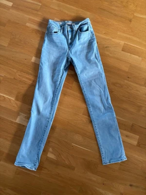 Ljusblå raka jeans - Säljer ett par ljusblå levis jeans med rak passform och klassisk femficksdesign. Jeansen har hög midja och är tillverkade i ett mjukt denimtyg. Perfekta för en avslappnad och trendig look. Måtten för byxorna är W26 och L32.