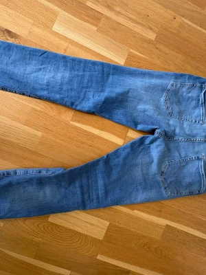 Blå slim fit jeans med raka ben - Snygga blå jeans i slim fit-modell med raka ben och klassiska bakfickor. Jeansen har en ljus tvätt och är tillverkade i ett mjukt denimtyg som ger en skön känsla. Perfekta för en avslappnad och trendig stil.