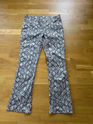 Ormmönstrade bootcut jeans Weekday - Säljer ett par gråa bootcut jeans från Weekday med ormmönster. Jeansen har hög midja och utsvängda ben, vilket ger en riktigt snygg retrovibe. Materialet är mjukt och stretchigt för extra komfort. Perfekta för dig som vill sticka ut lite extra!