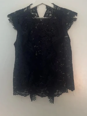 Svart spetsblus med kort ärm - Säljer en svart blus i spets med korta ärmar och rund hals. Blusen har fina spetsdetaljer över hela plagget och en lätt transparent look. Perfekt för dig som gillar en elegant och trendig stil.