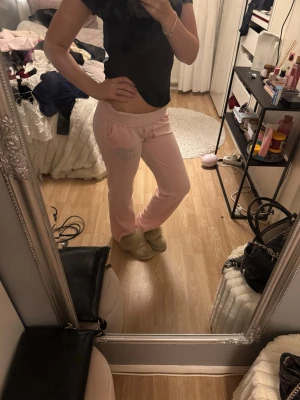 Ljusrosa mjukisbyxor med strassdetalj - Säljer ett par ljusrosa juicy mjukisbyxor med bred resår i midjan och fickor på sidorna. Byxorna har en snygg strassdetalj på ena sidan och baktill. Perfekta för chill dagar hemma eller när du vill vara extra comfy.