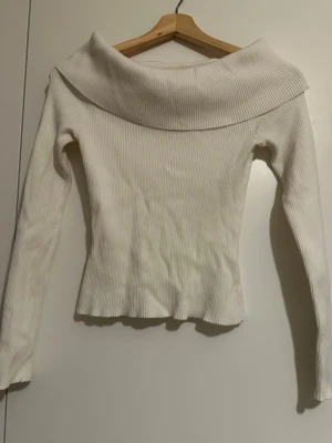 Vit ribbad offshoulder topp - Snygg vit ribbad topp med offshoulder-krage och långa ärmar. Perfekt för dig som vill ha en stilren och trendig look. Materialet är stretchigt och sitter snyggt på kroppen.