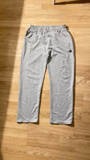 Grå välanvända mjukisbyxor från Adidas, strl M - Säljer ett par klassiska grå mjukisbyxor från Adidas med resår i midjan och raka ben. Dom är perfekta att ha som hemma byxor och är i storlek Medium(dam). Är använda väl och har 5st vita små färgfläckar här och där på byxorna(se bild 3,4,5,6) och ett litet handavtryck på framsidan just ovanför Adidas märket(se bild 3). Dom är mycket bekväma och har snygg passform då dom är raka i benen. Samt är dom högmidjade. Är i bra längd på mig och är ca 163cm. Säljes pga använder inte något mer☺️🙌🏻