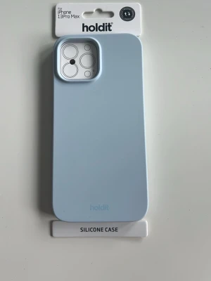 Ljusblått silikonskal Holdit iPhone 13 Pro Max - Snyggt ljusblått silikonskal från Holdit som passar iPhone 13 Pro Max. Skalet är gjort i mjukt silikonmaterial som ger bra grepp och skydd mot stötar. Slimmad design med öppning för kamera och stöd för trådlös laddning. Perfekt för dig som vill ha en stilren look. Helt ny i orginalförpackning, aldrig använd!