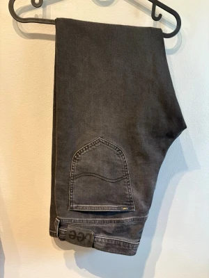Svarta Lee jeans med rak passform - Säljer ett par svarta jeans från Lee med klassisk rak passform. Jeansen har en unik bakficka med Lee-logga och är tillverkade i slitstarkt denimtyg. Perfekta för dig som gillar en enkel och stilren look.